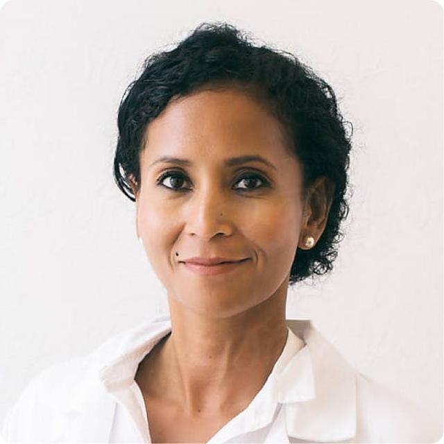 Portrait of a female healthcare provider in a white coat with short curly hair and a confident expression.